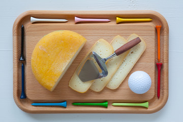 Block of tasty cheese on cutting board with a knife and golf tee