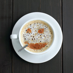 funny and bouncy joke Barista coffee maker/ cup of coffee with frothy and cinnamon smile, standing on a wooden table top view