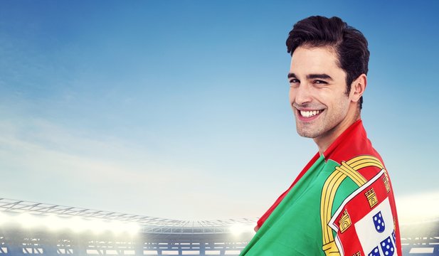 Athlete with portuguese flag wrapped around his body against large football stadium under bright blue sky