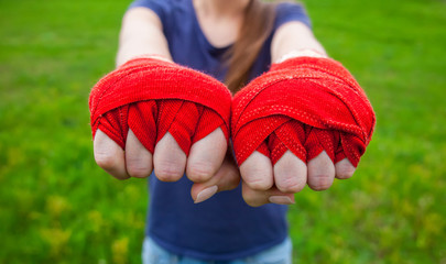 Girl athlete, boxer standing in the park and stretches both hands clenched into fists wrapped sport, red bandages Boxing forward. Preparation for training. The concept of sports and healthy lifestyle.