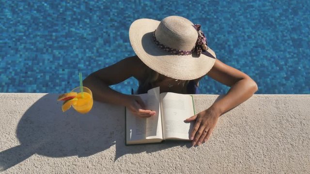 woman relaxing reading book in swimming pool top view