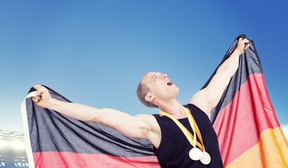 Athlete posing with olympic gold medals around his neck against large football stadium under bright blue sky