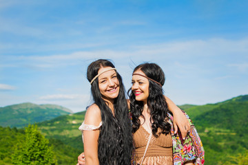 Two beautiful boho sisters hugging outdoors on sunny summer day