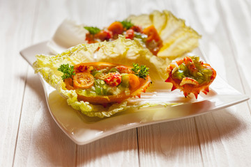 Exotic Shrimp salad served in n half a kiwano and leaves of the Chinese cabbage for summer party on wooden table, selective focus, copy space