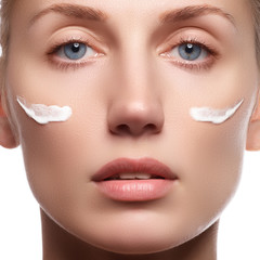 Beautiful face of young woman with cosmetic cream on a cheek. Sk