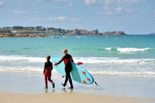 Père et fille marchent sur une plage de Bretagne où ils viennent de pratiquer le surf