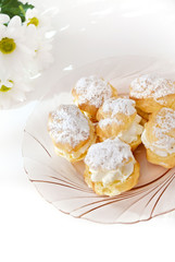 Cream puff or profiterole with filling and powdered sugar topping, isolated, against white background