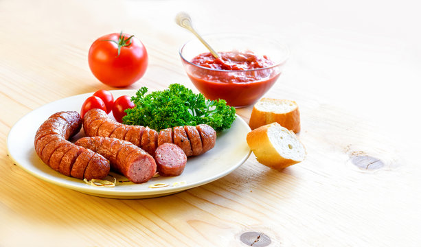 Roasted sausage with bread and vegetables served on white plate and wood board