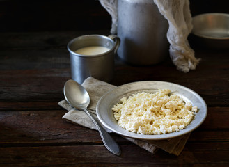 homemade cottage cheese in vintage aluminum bowl,  and water-can on a wooden background. rustic style