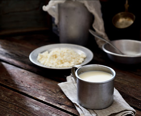Milk in vintage aluminum mug, a bowl of cottage cheese, a water-can. rustic style
