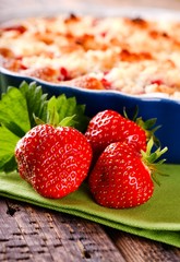 Three fresh red strawberries in front of fruit cake on green towel