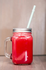 A watermelon smoothie in a mason jar with tube on wooden background