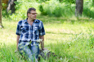 Portrait of man sitting on lawn of forest on stone