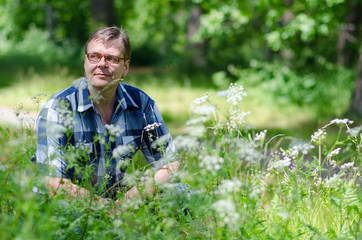 Smiling man sits on lawn of forest in sunny day