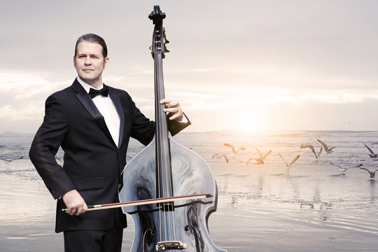 man with doublebass standing by the ocean