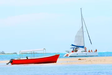 Schilderijen op glas Rode motorboot en catamaran op de Indische Oceaan in de buurt van het eiland Ile Aux Cerfs (Mauritius-eiland). Blauwe zee en strand in tropisch paradijs. © Kletr