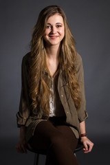 Beautiful blond girl with blue eyes on a gray background. She wears jacket and brown pants and white shirt. 