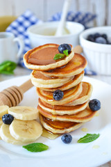 Small pancakes stacked with blueberries, banana and honey