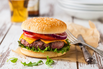 Homemade natural hamburger with cheese tomato and onion rings on a rustic table