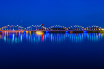 Illuminated railway bridge and reflection in Daugava river at tw