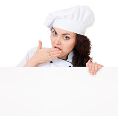 Shocked young woman cook or baker holding a blank signboard, isolated on white background