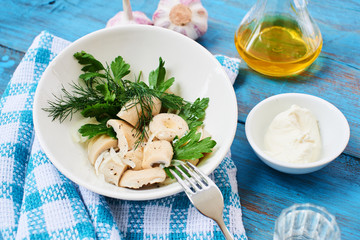 Salted mushrooms in a white plate, a bowl of sour cream and a jug of oil on a wooden table