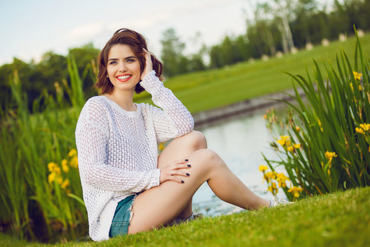 Outdoor photo of young woman near the pond. Beautiful tender woman with red hair posing in summer park.