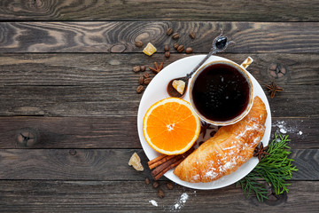 Continental breakfast - cup of hot coffee, croissant and orange. Tasty food on rustic wooden background. Top view, place for text.