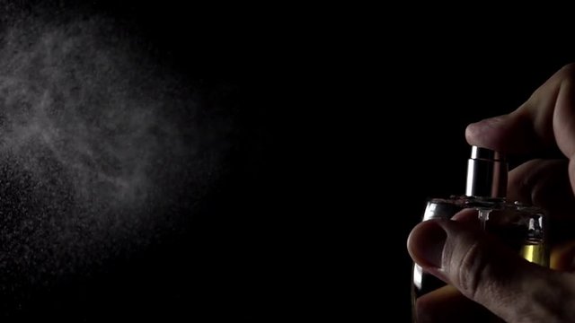Atomizing perfume against black background. Super slow motion shot at 500 fps