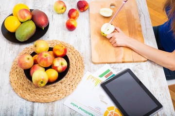 Young woman preparing fruit juice while getting online information about nutrition..