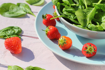 Fresh spinach salad with spinach and strawberries on wooden light pink table