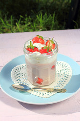 Fresh strawberries with fruit yoghurt and whipped cream on light pink wooden table