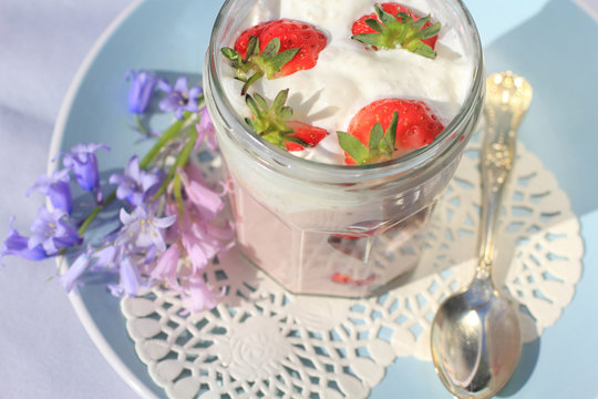 Fresh strawberries with fruit yoghurt and whipped cream on light pink wooden table