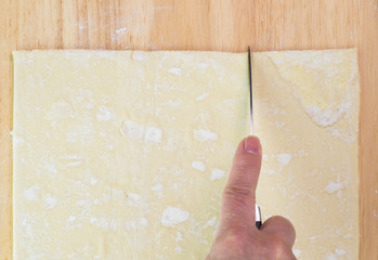 Cutting square pastry sheet with knife.