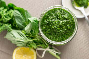 Basil pesto sauce with ingredients. Fresh homemade basil pesto sauce in a glass jar. Originally from italy, pesto is commonly made with basil and used as a sauce for pasta.