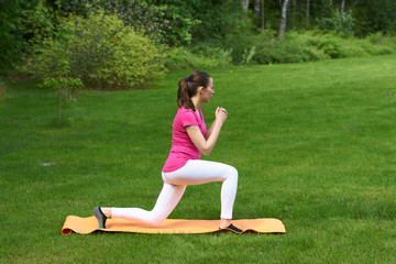 Naklejka na ściany i meble Sexy brown haired woman in pink t-shirt, white leggings, black socks with green stripers doing physical exercises for buttocks and legs on orange mat on grass in nature.