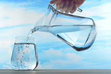 Fresh and clean drinking water being poured from jug into glass on sky background © amenic181