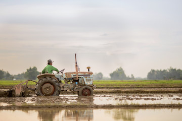 a senior male farmer smoking and sitting in a tractor during sunset time