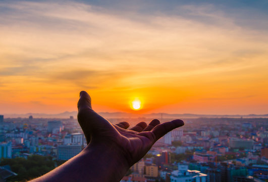 Hand holding sunset and city of background