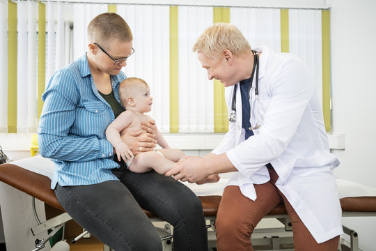 Mother Looking At Happy Mature Doctor Holding Baby's Legs