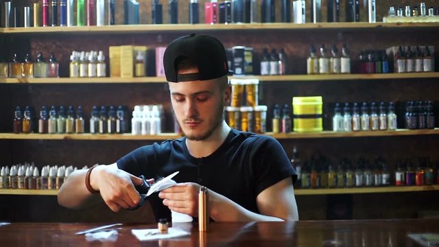 young seller in vape shop is installing cotton in atomizer show window in background