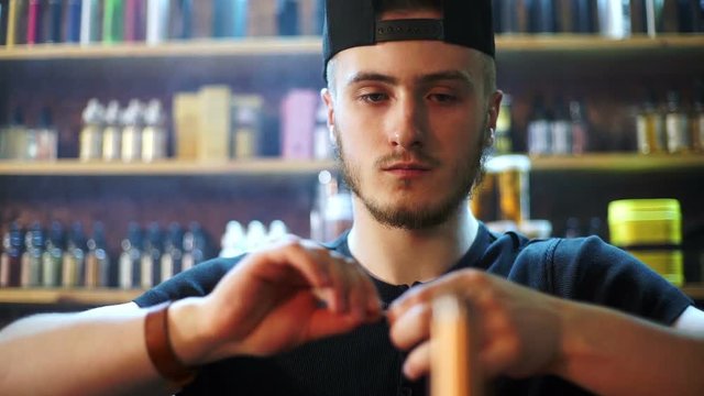 young seller in vape shop is installing cotton in atomizer show window in background