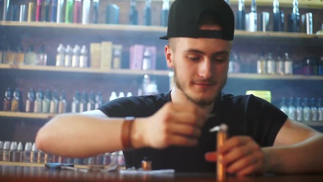young seller in vape shop is installing cotton in atomizer show window in background