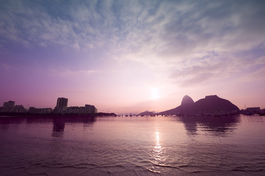 Colorful sunrise reflects on the calm surface of Botafogo Bay with a silhouette of Sugarloaf Mountain in Rio de Janeiro, Brazil