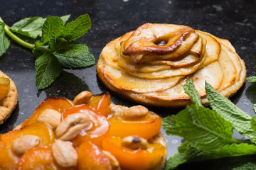 Tart with apricot and apple. Traditional french pie with fruits on dark marble background. Decorated almonds and mint leafs. Delicious dessert with copy space closeup.
