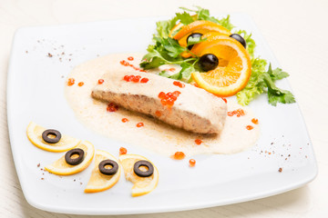 A piece of salmon with garnish and white sauce