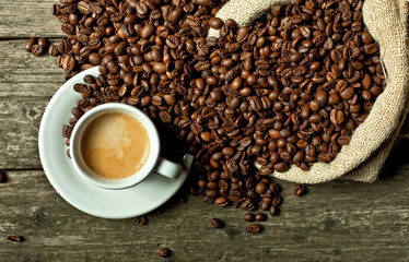  flat lay style image of an espresso coffee in a white cup on an old wooden planks background, jute bag with coffee beans.