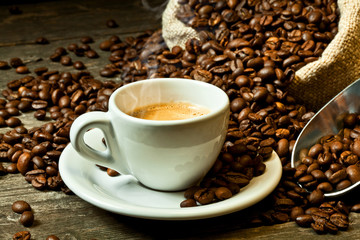 steaming white coffee cup, beans and jute bag wooden bottom