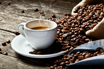 classic white cup and steaming coffee, with sack containing roasted beans on wooden background. warm and relaxing atmosphere. nobody around.