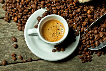 classic white cup and steaming coffee, with sack containing roasted beans on wooden background. warm and relaxing atmosphere. nobody around.